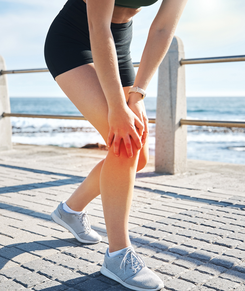 Photo of a woman in jogging clothes standing on a pier, clutching her knee