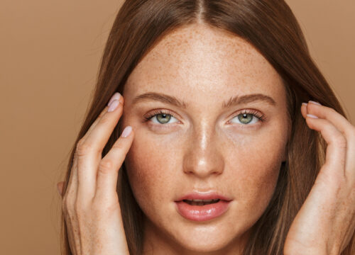 Photo of a woman with freckles touching her face