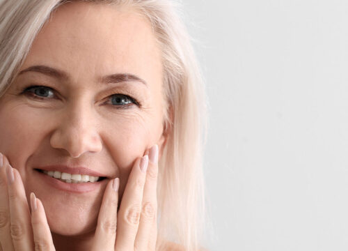 Photo of a smiling older woman touching her face