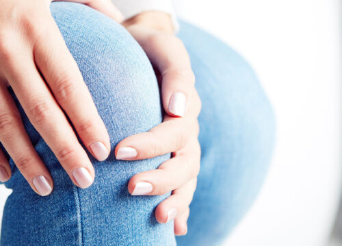 Photo of a woman in jeans clutching her knee in pain